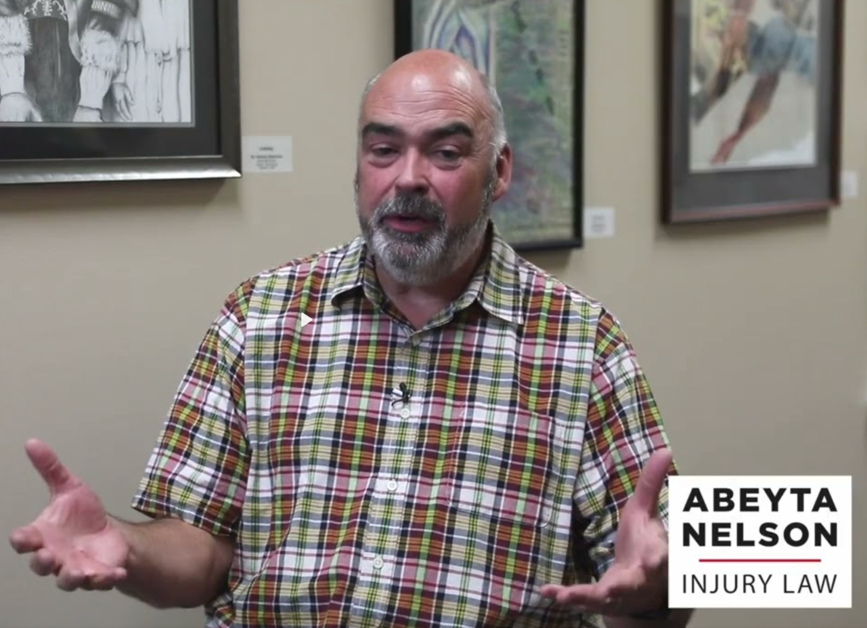 A middle-aged man with a bald head and beard wearing a plaid shirt gestures while speaking, seated in front of framed artwork. "Abeyta Nelson Injury Law" appears in the corner.