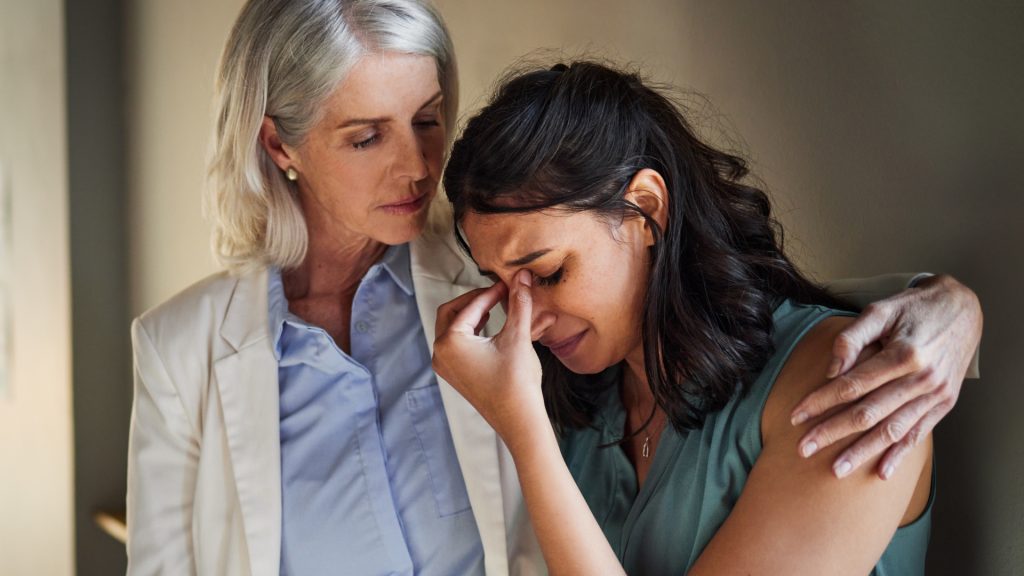 An older woman comforts a younger woman who is crying, with her arm around her in a supportive gesture.