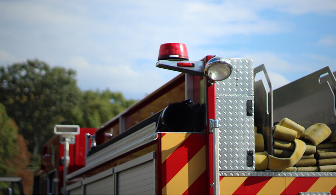 Primer plano de un camión de bomberos con una luz de emergencia roja, mangueras y equipo guardado en el lateral, en el exterior en un día despejado.
