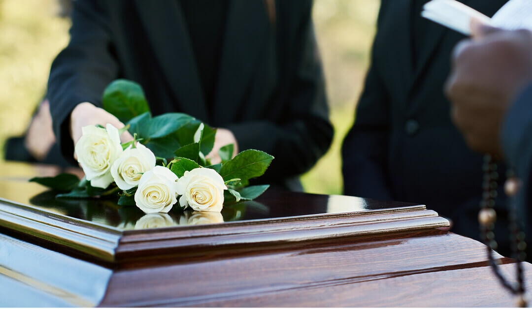 Una persona coloca un ramo de rosas blancas sobre un ataúd de madera cerrado durante un servicio funerario.