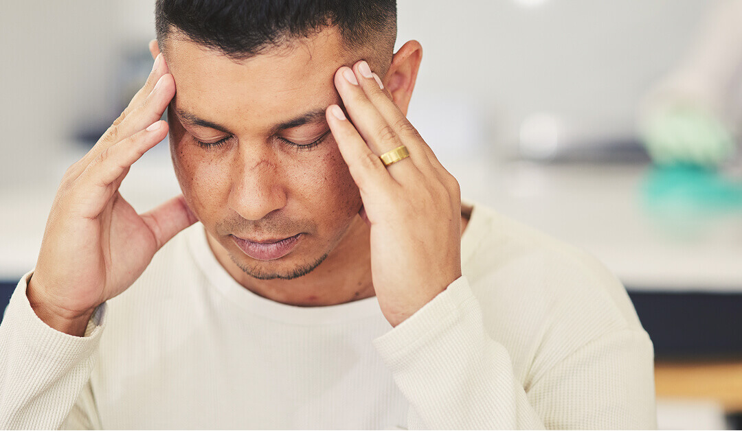 Un hombre con los ojos cerrados se toca las sienes con ambas manos, como si estuviera dolorido o profundamente pensativo.